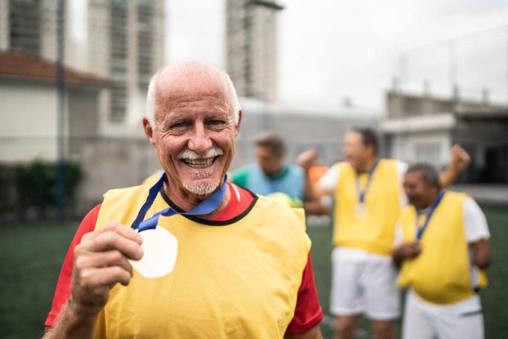 a senior man holding up his medal on the soccer field